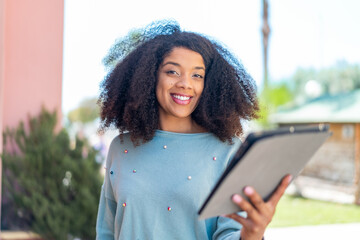 Young African American woman holding a tablet at outdoors with happy expression