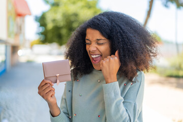 Young African American woman holding a wallet at outdoors celebrating a victory