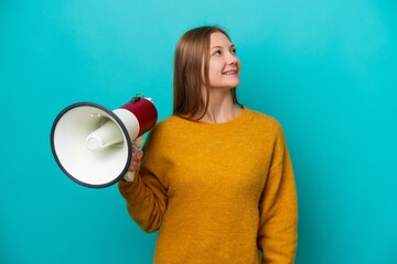 Young Russian woman isolated on blue background holding a megaphone and looking up while smiling