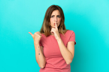 Young caucasian woman isolated on blue background pointing to the side and doing silence gesture