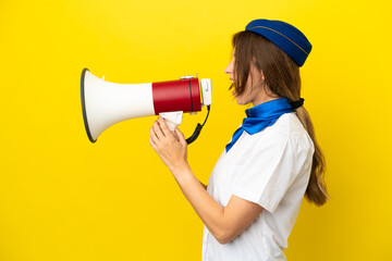 Airplane stewardess woman isolated on yellow background shouting through a megaphone