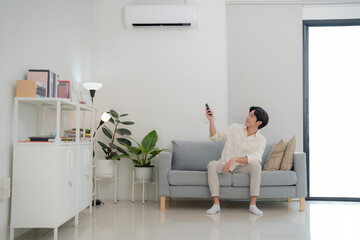 Young man enjoying comfort using remote control for air conditioning at home
