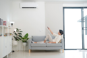 Young man enjoying comfort using remote control for air conditioning at home