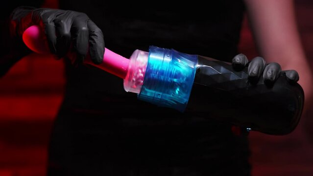 Girl in a black dress and black gloves inserts an artificial pink dildo into an automatic telescopic male masturbator. On a red background. Male massager. Sex shop Adult store, toys for two
