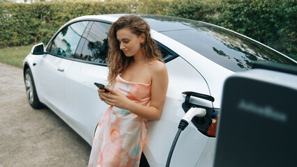 Young woman use smartphone to pay for electricity at public EV car charging station in nature....
