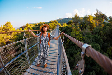 Girl with a backpack. a young woman in a hat and with a backpack walks along a suspension bridge...