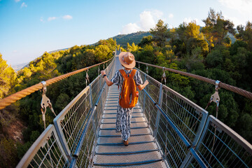 Girl with a backpack. a young woman in a hat and with a backpack walks along a suspension bridge...