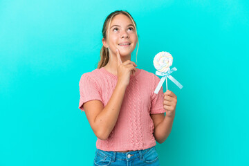 Little Caucasian girl holding a lollipop isolated on blue background thinking an idea while looking...