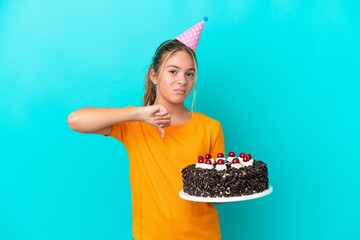 Little caucasian girl holding birthday cake isolated on blue background showing thumb down with...