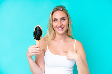 Young caucasian woman with hair comb isolated on blue background with surprise facial expression