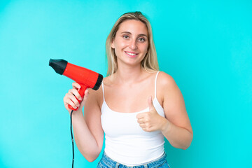 Young caucasian woman holding a hairdryer isolated on blue background with thumbs up because...