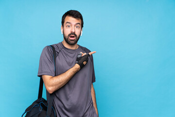 Young sport man with beard over isolated blue background surprised and pointing side