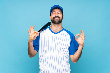 Naklejka premium Young man playing baseball over isolated blue background in zen pose