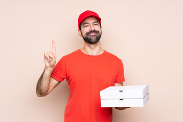 Young man holding a pizza over isolated background showing and lifting a finger in sign of the best