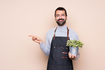 Man holding a plant over isolated background pointing finger to the side