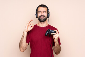 Man playing with a video game controller over isolated wall in zen pose