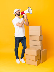 Full-length shot of delivery man among boxes over isolated yellow background shouting through a...