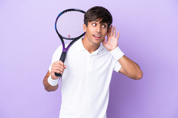 Handsome young tennis player man isolated on ocher background listening to something by putting...