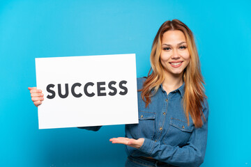 Teenager girl over isolated blue background holding a placard with text SUCCESS with happy...
