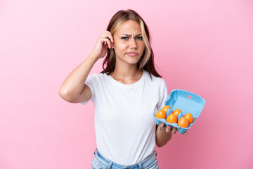 Young Russian woman holding eggs isolated on pink background having doubts