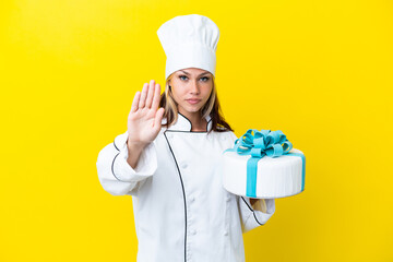 Young Russian pastry chef woman with a big cake isolated on yellow background making stop gesture
