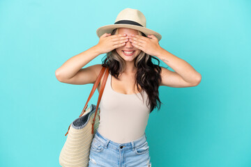 Teenager Russian girl with pamel and beach bag isolated on blue background covering eyes by hands