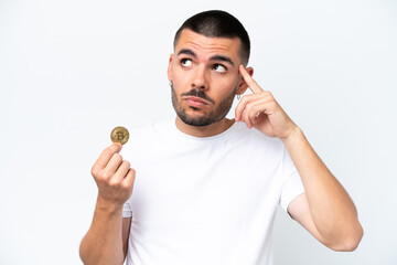 Young caucasian man holding a bitcoin isolated on white background having doubts and thinking