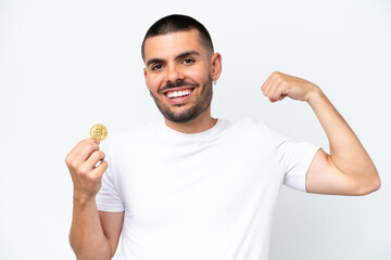 Young caucasian man holding a bitcoin isolated on white background doing strong gesture