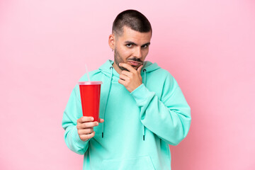 Young caucasian man holding soda isolated on pink background thinking