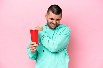 Young caucasian man holding soda isolated on pink background suffering from pain in shoulder for...