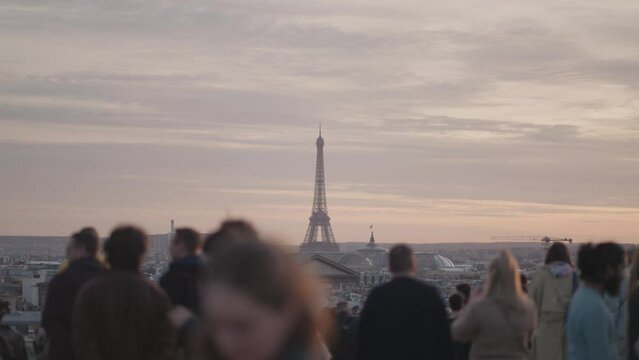 Unrecognizable Tourists on the rooftop of Galeries Lafayette Haussmann enjoying the sunset with the iconic Eiffel Tower and the city buildings of Paris in the background