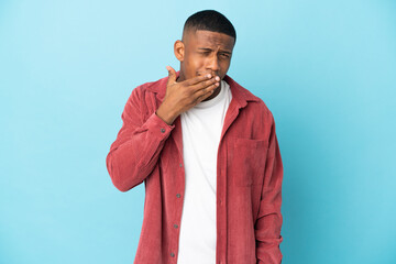 Young latin man isolated on blue background yawning and covering wide open mouth with hand