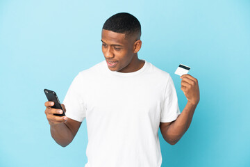 Young latin man isolated on blue background buying with the mobile with a credit card