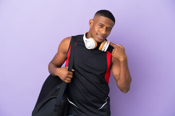 Young sport latin man with sport bag isolated  on purple background giving a thumbs up gesture