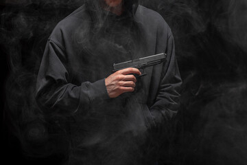 Young man in a black hoodie holding a pistol on a smokey black background