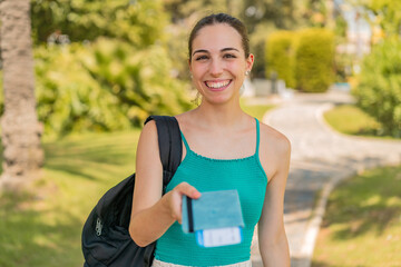 Young pretty woman at outdoors holding a passport with happy expression