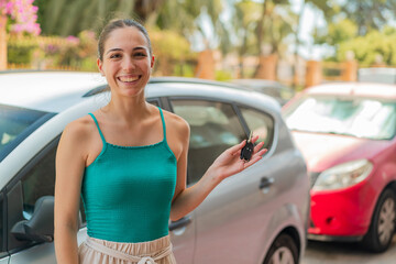 Young pretty woman at outdoors holding car keys with happy expression