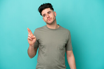 Young caucasian man isolated on blue background with fingers crossing and wishing the best