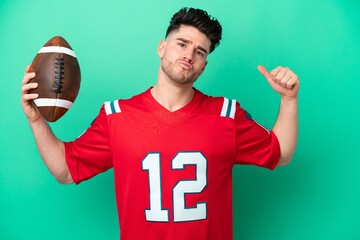 Young caucasian man playing rugby isolated on green background doing strong gesture