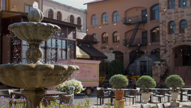 Charming outdoor cafe with decorative water fountain in European style courtyard, adorned with plants and flowers, surrounded by rustic buildings and serene atmosphere for relaxation