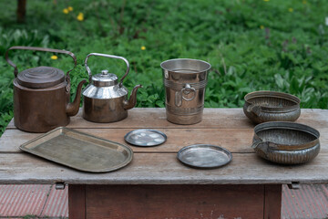 Ancient kettles, bowls, trays on an old wooden table.