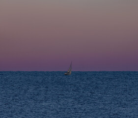 Racing sailboat sailing at dawn in a calm Mediterranean sea with the dawn sun about to rise...