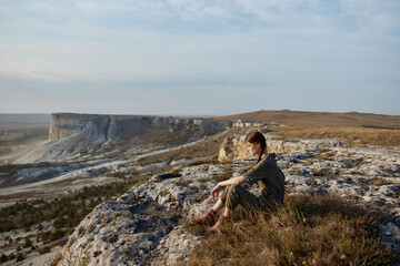 Naklejka premium Woman sitting on cliff overlooking valley and mountains in inspiring travel adventure destination concept