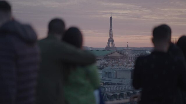 Unrecognizable Tourists on the rooftop of Galeries Lafayette Haussmann enjoying the sunset with the iconic Eiffel Tower and the city buildings of Paris in the background