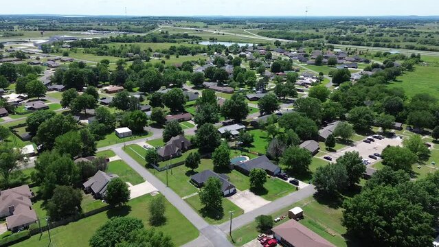 Quiet residential SW 4th Steet in Checotah, McIntosh County, Oklahoma, row of single-family houses, large backyard toward Interstate I-40 with water tower in background, sunny days flyover view. USA