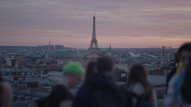 Unrecognizable Tourists on the rooftop of Galeries Lafayette Haussmann enjoying the sunset with the iconic Eiffel Tower and the city buildings of Paris in the background