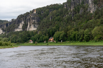 A river with a house on the bank. The house is small and brown. The water is calm and clear