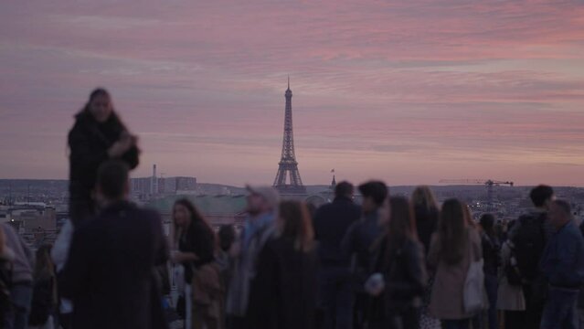 Unrecognizable Tourists on the rooftop of Galeries Lafayette Haussmann enjoying the sunset with the iconic Eiffel Tower and the city buildings of Paris in the background