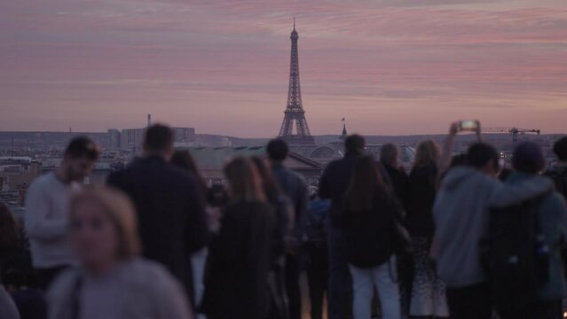 Unrecognizable Tourists on the rooftop of Galeries Lafayette Haussmann enjoying the sunset with the iconic Eiffel Tower and the city buildings of Paris in the background