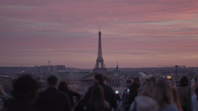 Unrecognizable Tourists on the rooftop of Galeries Lafayette Haussmann enjoying the sunset with the iconic Eiffel Tower and the city buildings of Paris in the background